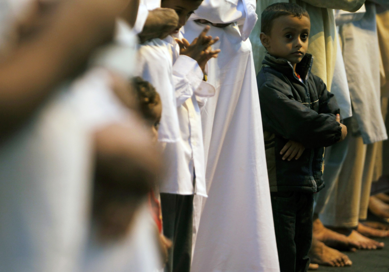 A boy stands beside his father, as Muslim pilgrims pray in 